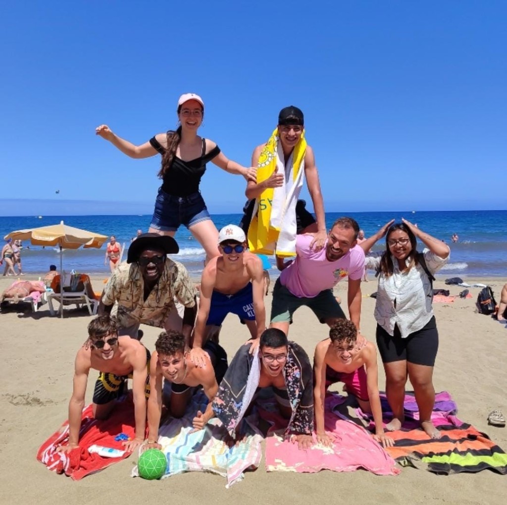 A diverse group of young people and adults forming a human pyramid together on a sunny beach