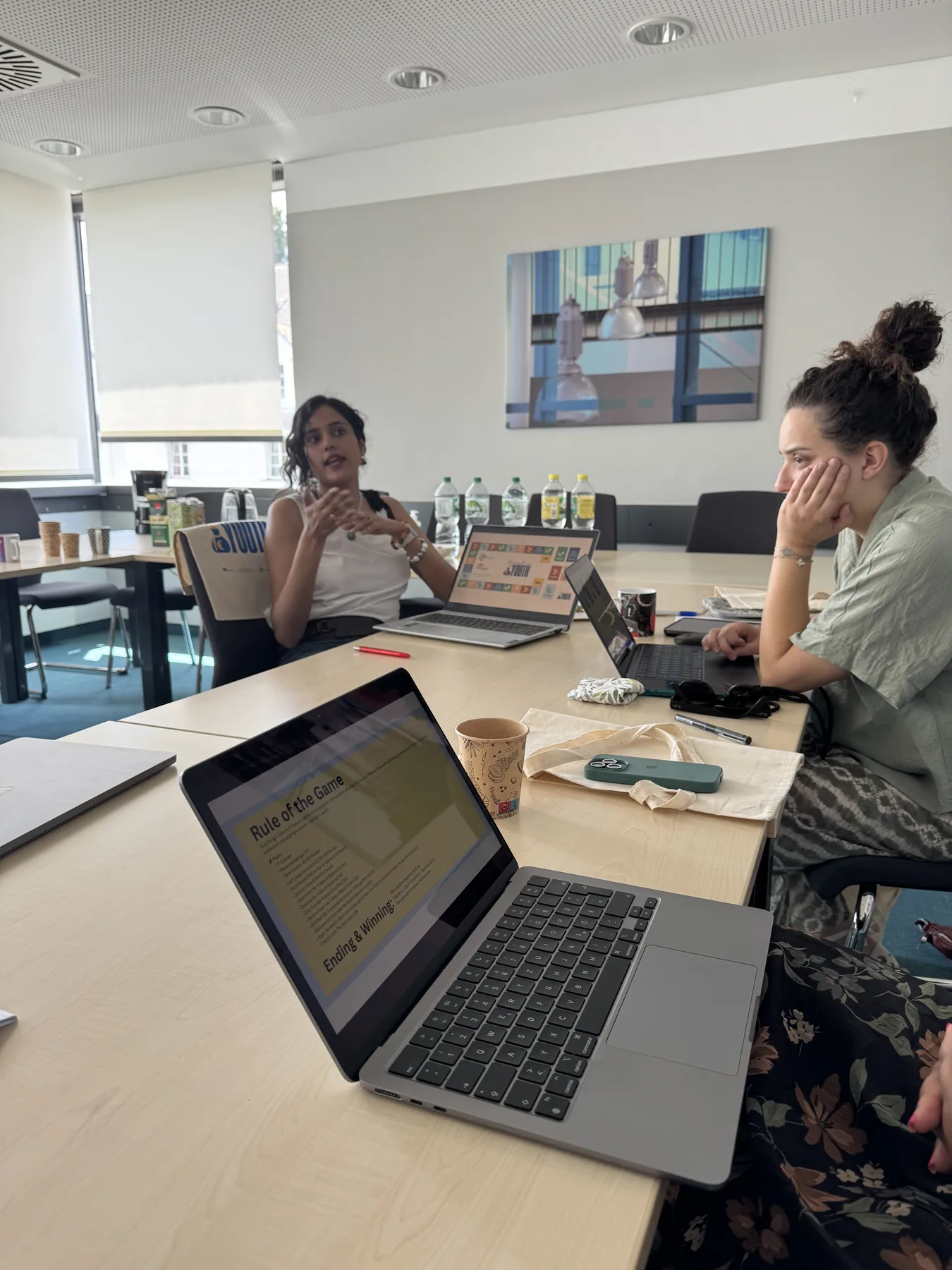 Partners discussing the Invest in Youth board-game concept with Rules of the Game notes visible on a laptop.